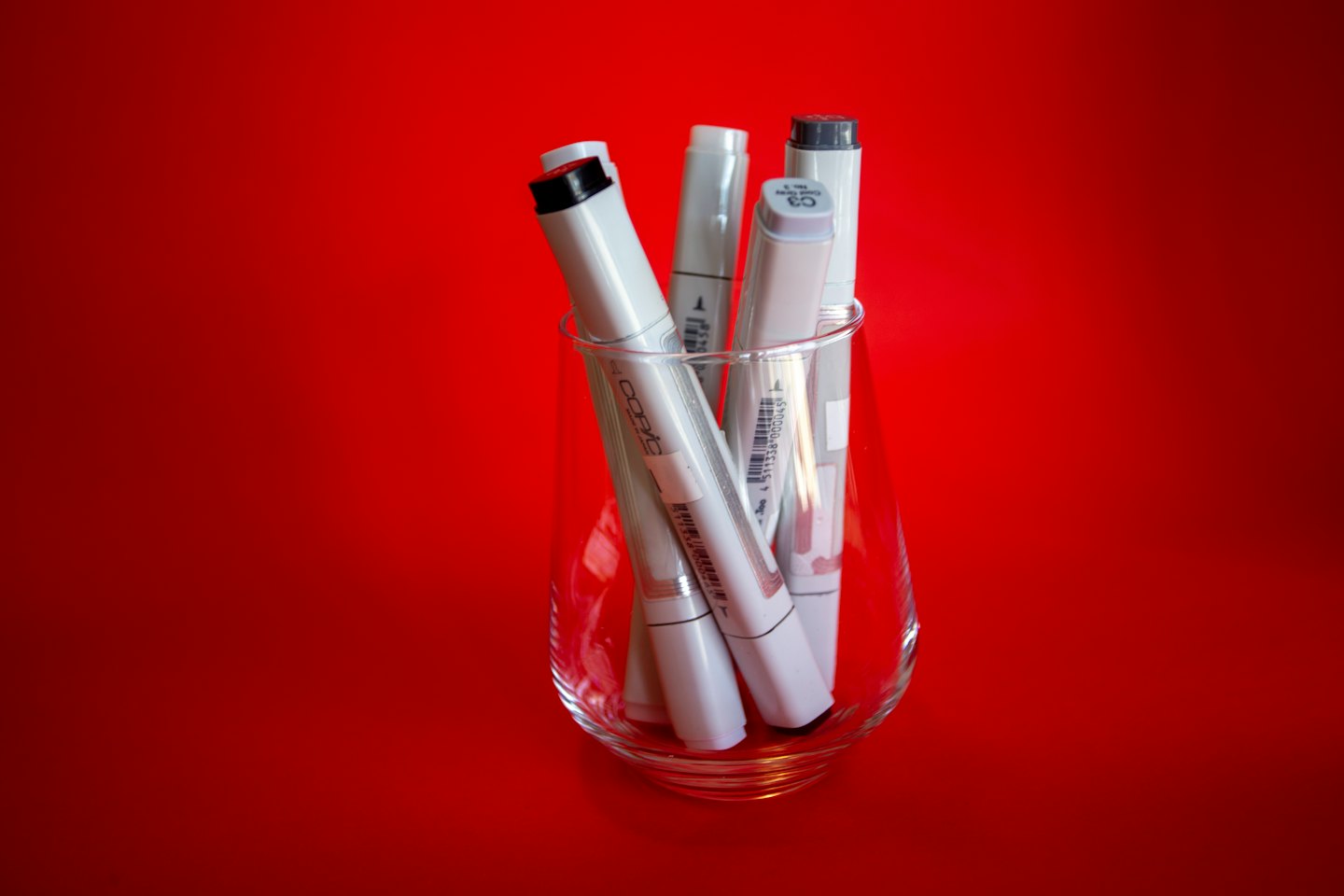 Gray art markers standing inside a clear glass container.