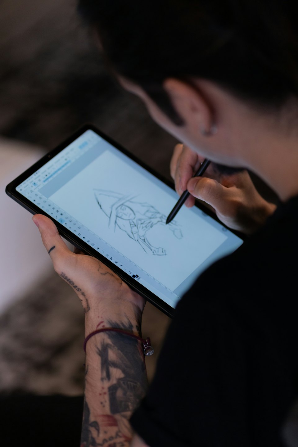 Person with tattoos draws on a digital tablet with a stylus.