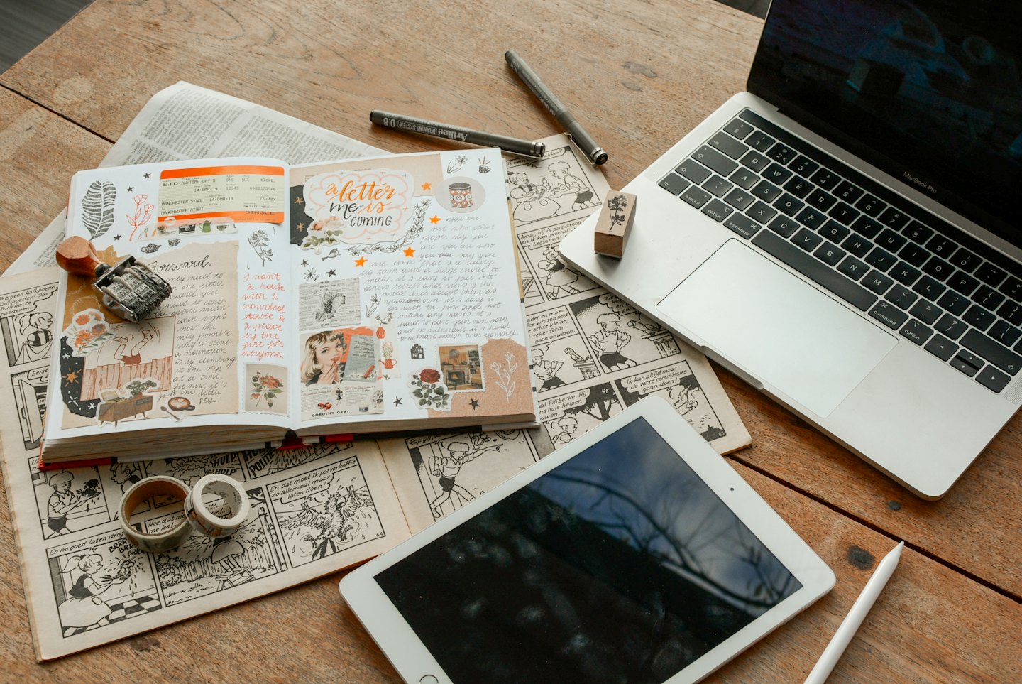 Laptop and tablet rest on a journal filled with stickers.